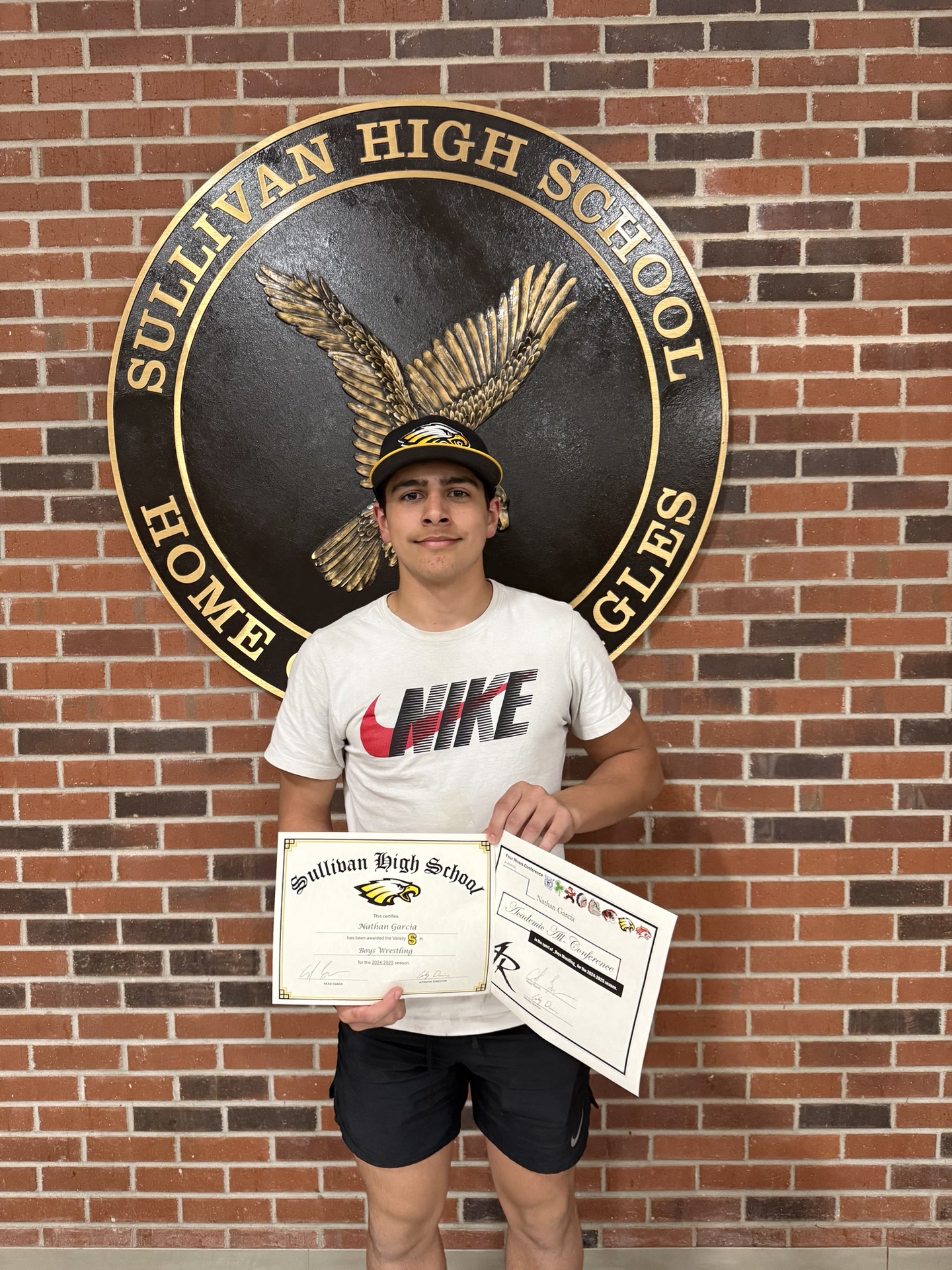 Nathan Garcia holding certificates in front of Sullivan High School eagle seal